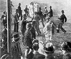 A cricketer leading his team off the field watched by a crowd