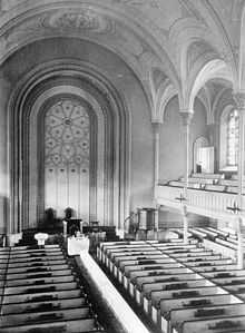 A black-and-white image of a church interior, seen from the gallery. The gallery and vaulted ceiling are supported by small columns.