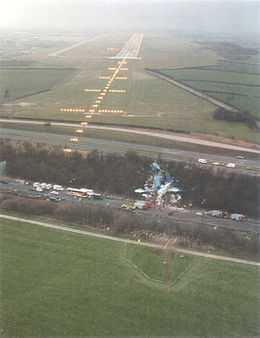 The wreck of an airliner lies between roads roughly 100m to the right of approach lights and several hundred metres in front of a runway. The wreck is broken into three large pieces, a nose section, a central section and a tail section. The tail section is turned around, the horizontal stabilizers resting in front of the wings of the central section.