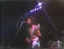 Garry Shider in 1976 touring with Parliament-Funkadelic. He is in his trademark diaper look. The is 23 years old and playing guitar, standing in front of a microphone and preparing to sing.