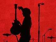 A man standing in front of a red background with a guitar in his hand.