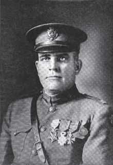 Head and shoulders of a middle-aged man in military uniform with a strap across his chest, four medals on his left breast, and a peaked cap.