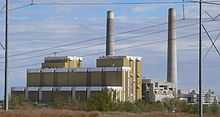 Multistory building with two large smokestacks; power lines in foreground