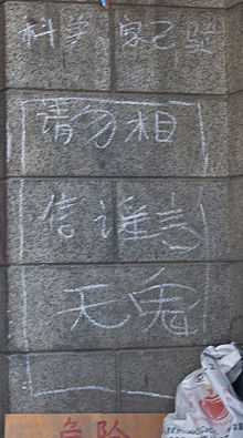 White Chinese characters chalked on a stone wall. Two at the bottom are larger than the others