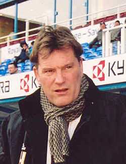 A middle-aged white man, in a jacket with a scarf wrapped around his neck