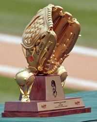 A trophy sits on a green table topped by a golden baseball glove flanked by two golden baseballs.