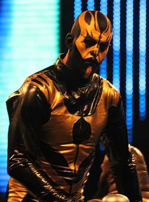 A Caucasian male adult with yellow and black face paint and wrestling attire.