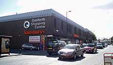 A 1970s monolithic shopping centre, mostly grey/brown in colour. In the foreground the busy High Street with a number of travelling cars.