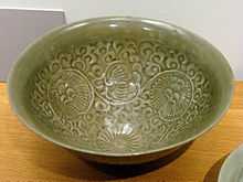 A green bowl with a pattern of circular flowers with small, thin petals set over a background of vines glazed into it.