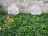 Two graves and two gravestones side by side; heading behind a bed of green leaves, bearing the remains of Vincent and Theo Van Gogh, where they lie in the cemetery of Auvers-sur-Oise. The stone to the left bears the inscription: Ici Repose Vincent van Gogh (1853–1890) and the stone to the right reads: Ici Repose Theodore van Gogh (1857–1891)