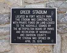 Set against a natural stone wall, a black plaque with silver text reads, "Greer Stadium. Located in Fort Negley Park this stadium was constructed with private funds on land leased to the Nashville Sounds by the Metropolitan Board of Parks and Recreation of Nashville and Davidson County. The stadium was opened on April 25, 1978.