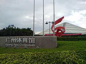 An outer view of indoor stadium/complex with conical roof, greenery in front, and an inscription – "Guangzhou Gymnasium" in both English and Chinese.