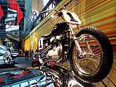 A pristine 1960s Harley-Davidson scrambler style motorcycle mounted as if riding over a rolling reflective steel surface.