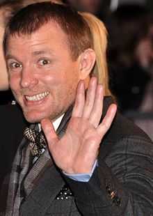 Guy Ritchie smiling and waving his hand