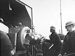 Gunners wearing steel helmets load a shell into a large calibre weapon