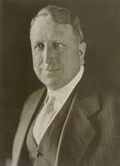 A black-and-white photograph of a middle-aged man in a business suit.