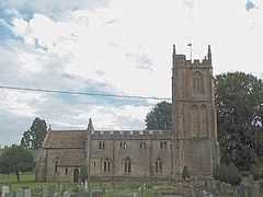 Stone building with arched windows. Prominent square tower to the right hand end. In the foreground are gravestones in grassy area.