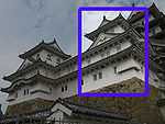 A three-storied castle tower with white walls and a dark roof on a platform of unhewn stones. It is connected to a two-storied structure.