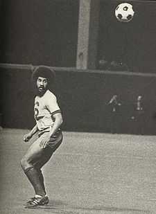 A black-and-white photograph of a man of African-Caribbean descent, wearing soccer attire, in the motion of turning to his left with his eyes on the ball.