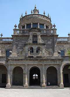 Entrance to a major stone building with colonnades and bells above the main entrance.