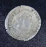 A silver coin in the centre a helmeted head surrounded by a circle of inscription with edging between that and the rim.