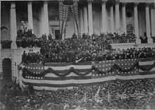 Photograph of crowd in front of Capitol building decorated with patriotic bunting
