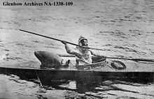 black and white image of an  Inuit hunter seated in a kayak holding a harpoon