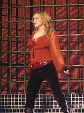 A blonde woman wearing a red shirt and dark pants is performing