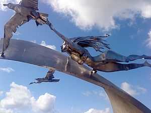 Shiny steel sculpture of woman gliding over a wave along with two seagulls