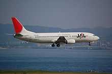 A Boeing 737-400 aircraft painted in new JAL corporate livery with a skyline background