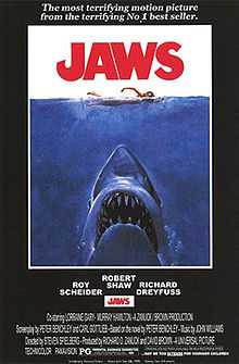 Movie poster shows a woman in the ocean swimming to the right. Below her is a large shark, and only its head and open mouth with teeth can be seen. Within the image is the film's title and above it in a surrounding black background is the phrase "The terrifying motion picture from the terrifying No. 1 best seller." The bottom of the image details the starring actors and lists credits and the MPAA rating.