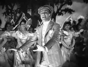 Cagney on stage and in costume, singing and dancing while the cast watches.