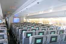 Interior view. Seats are separated by two aisles, in 3-4-3 configuration. A TV is positioned towards the front of aircraft.