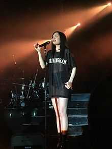 Jessie J with her hair down sings into a microphone on tour