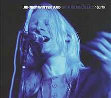 Close-up of Johnny Winter, singing and playing a guitar, with blue lighting