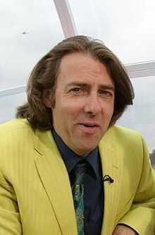 A man with brown hair sits in a yellow suit