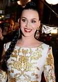 Katy Perry in a white and golden dress looking towards her right and smiling