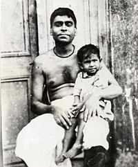 A middle-aged Indian man with bare chest sitting with a child on his lap