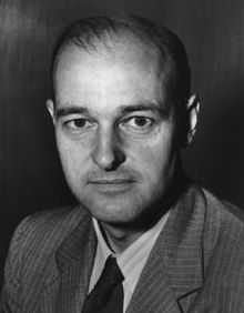 Head and shoulders portrait of a balding man, wearing a suit and tie.