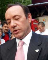 A close-up image of a man sporting a black suit and pink tie.