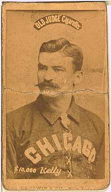 A baseball player is shown sitting, facing slightly left of the camera.