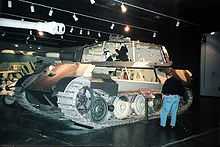 A side view of a large turreted tank in a museum, with sections of its superstructure and turret cut away.