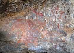 A picture of several red engravings depicting people hunting large animals on a cave wall.