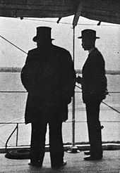 Kruger viewed in silhouette from behind, Bredell to his right. Kruger is wearing his trademark top hat.