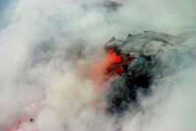 Photo showing clouds of steam surrounding lava that is partly black and partly glowing orange