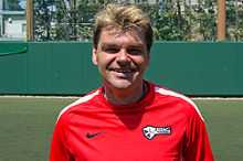 A Caucasian male adult with light brown colored hair and wearing a top red training clothes with white stripes on the shoulder.