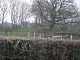 A flat topped grassy mound behind a barbed wire fence and hedgerow