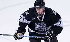 Young male ice hockey player in full gear, including a face mask, skates toward the camera with a determined expression as he looks past the camera.