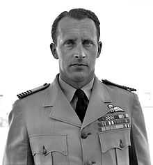 Outdoor head-and-shoulders portrait of a caucasian man in dark tie, light shirt, and light jacket with pilot's wings and medal ribbons on left-breast pocket