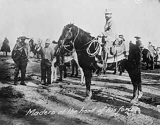 A black-and-white photo of a man, Francisco Madero, on horseback. Other men stand in background.